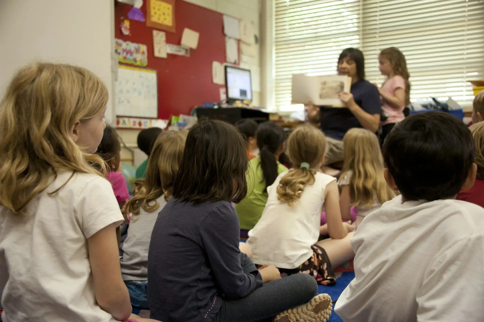A teacher reading to a class of children sitting on the floor