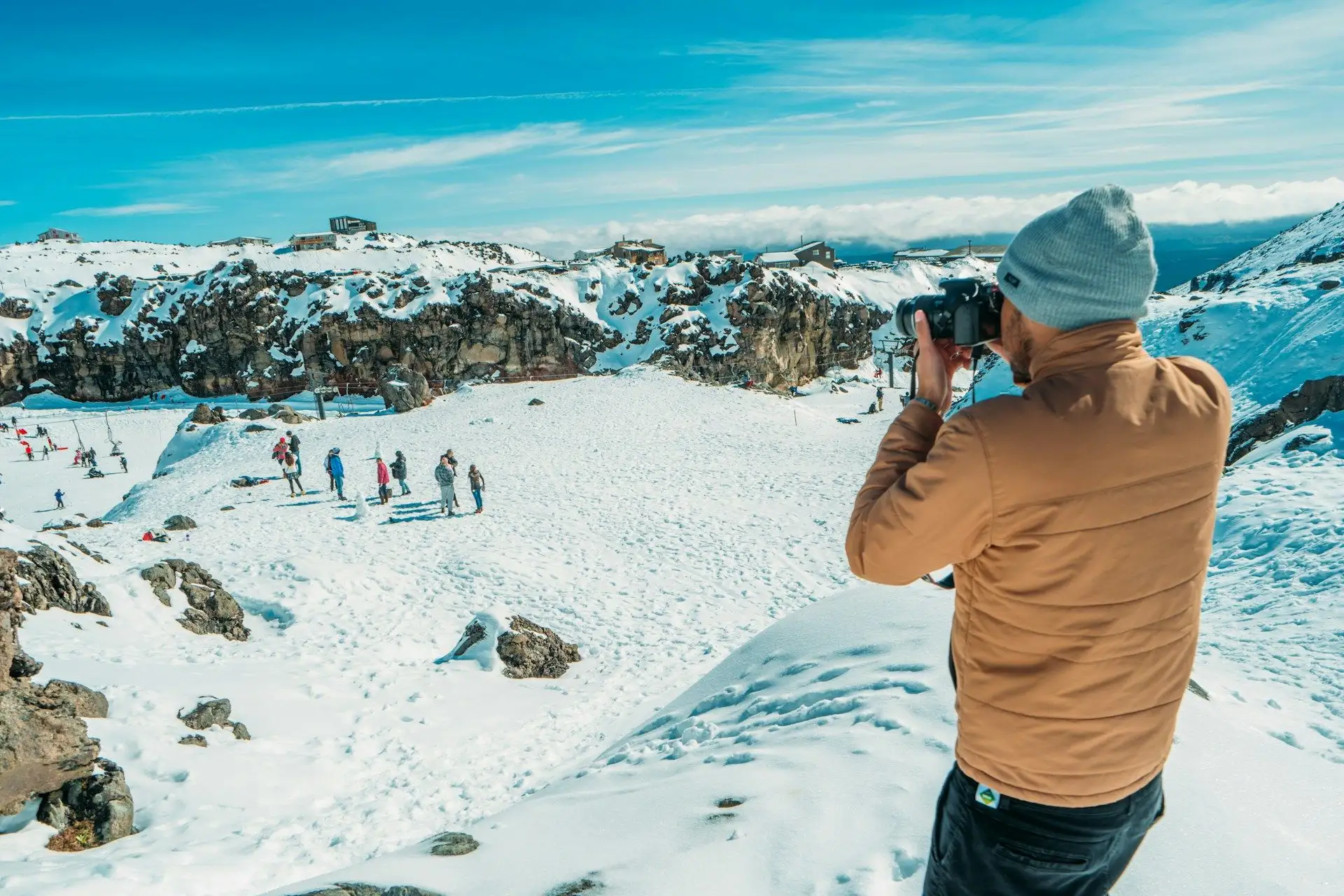 A visitor photographing the view from a snowy ridge in the Southern Alps