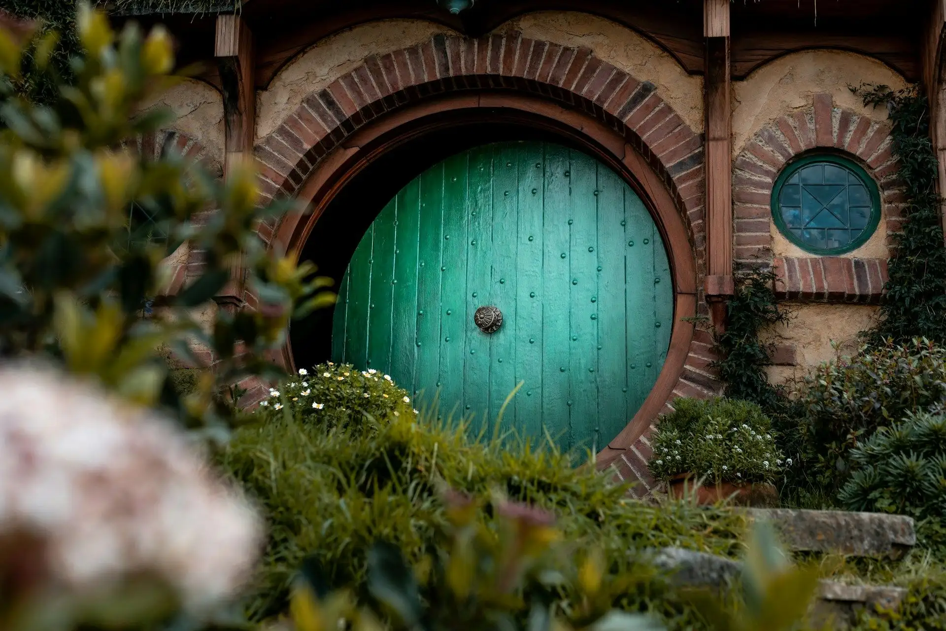 A turquoise round hobbit door framed by flowers at Hobbiton