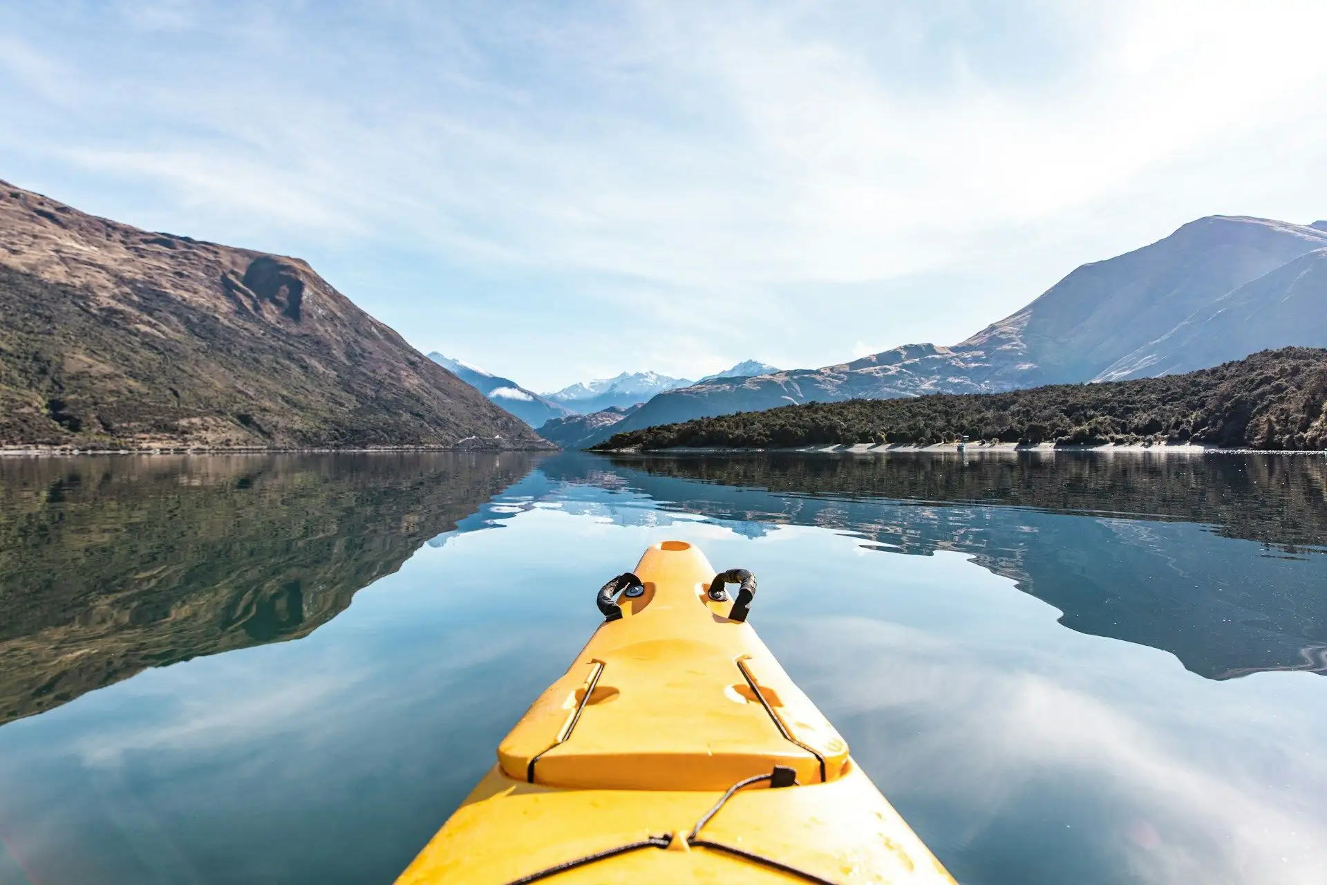 The bow of a yellow kayak on mirror-calm water below the mountains at Lake Wanaka