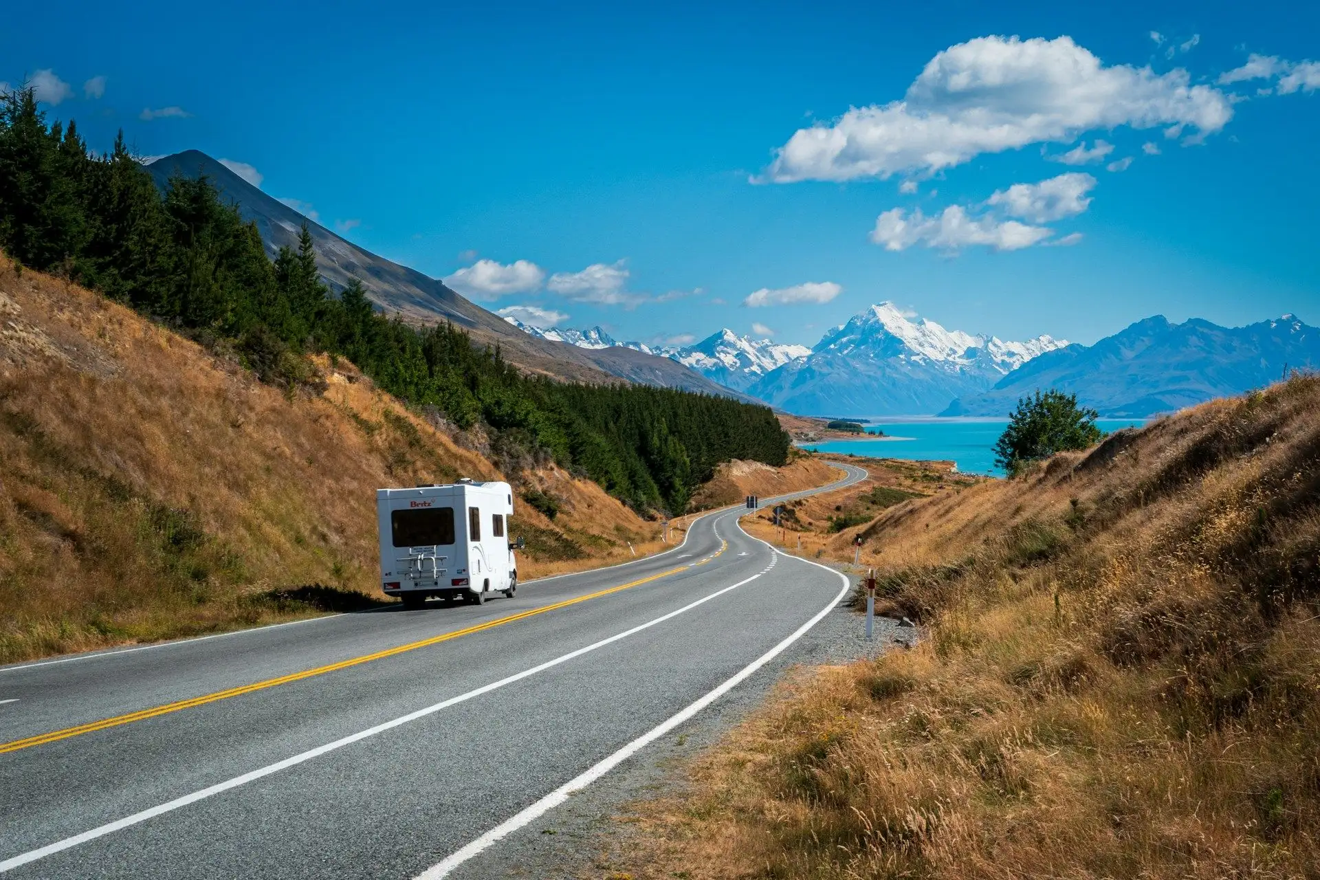 A campervan on the winding road above turquoise Lake Pukaki under a blue sky