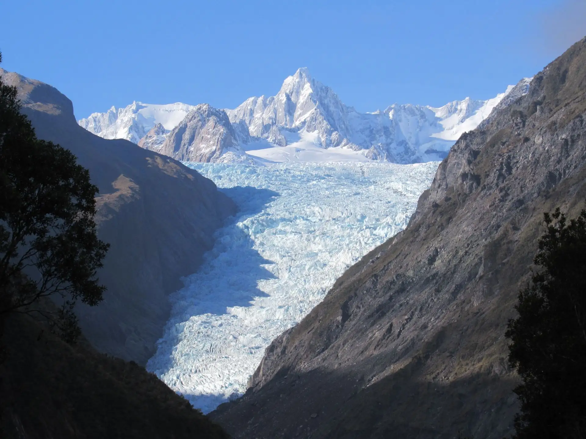 A glacier flowing between steep valley walls below snowy peaks