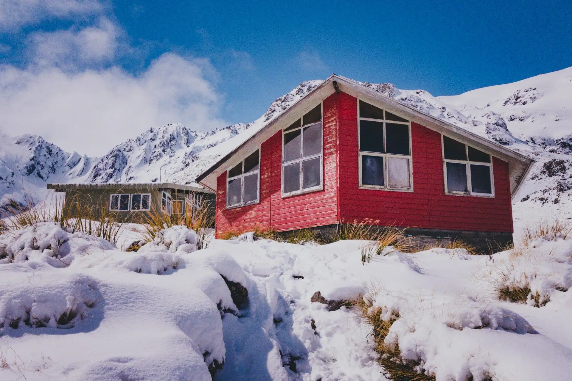 A red alpine hut in fresh snow under a bright blue sky