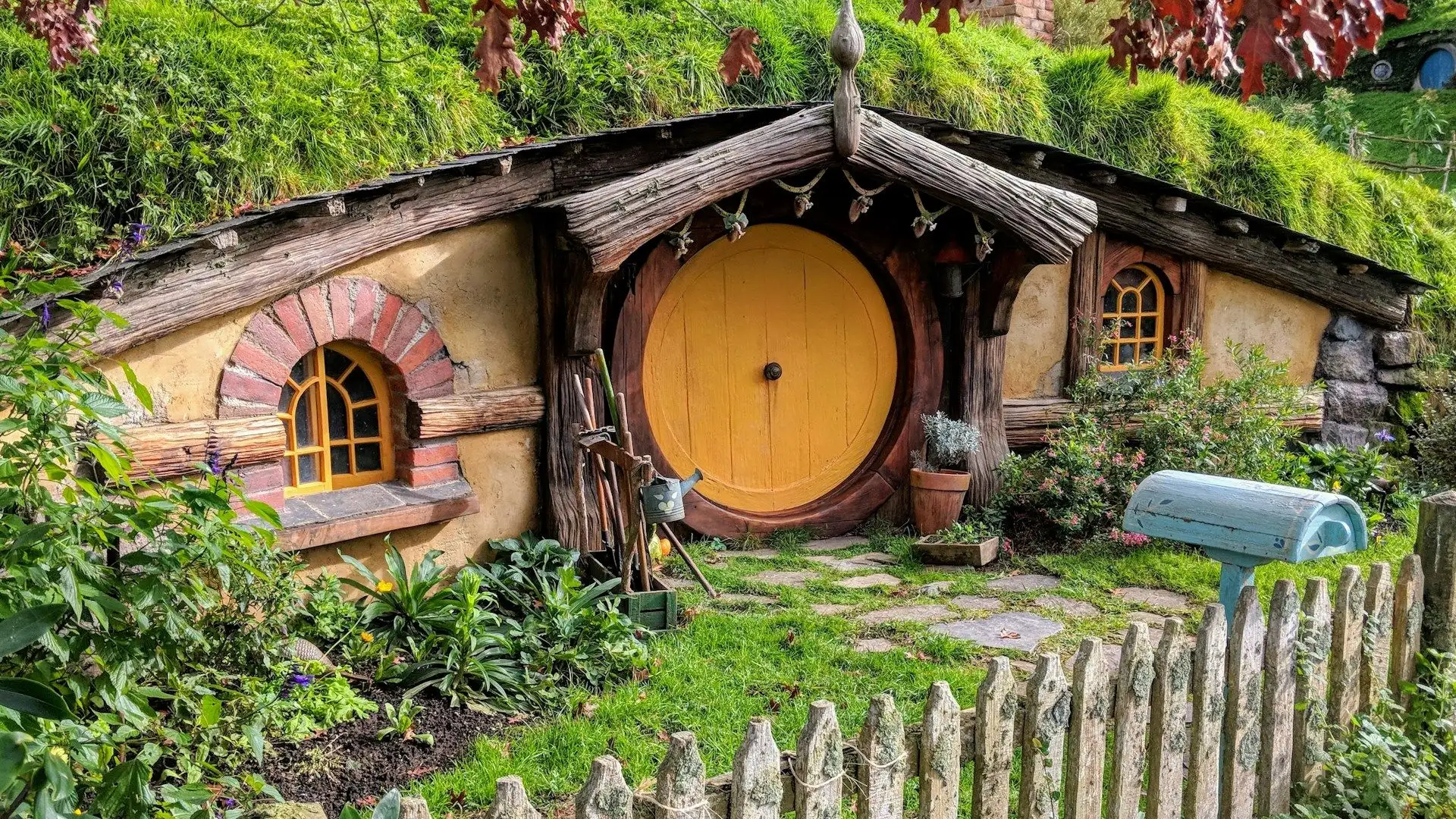 A yellow-door hobbit hole with a picket fence and letterbox at Hobbiton