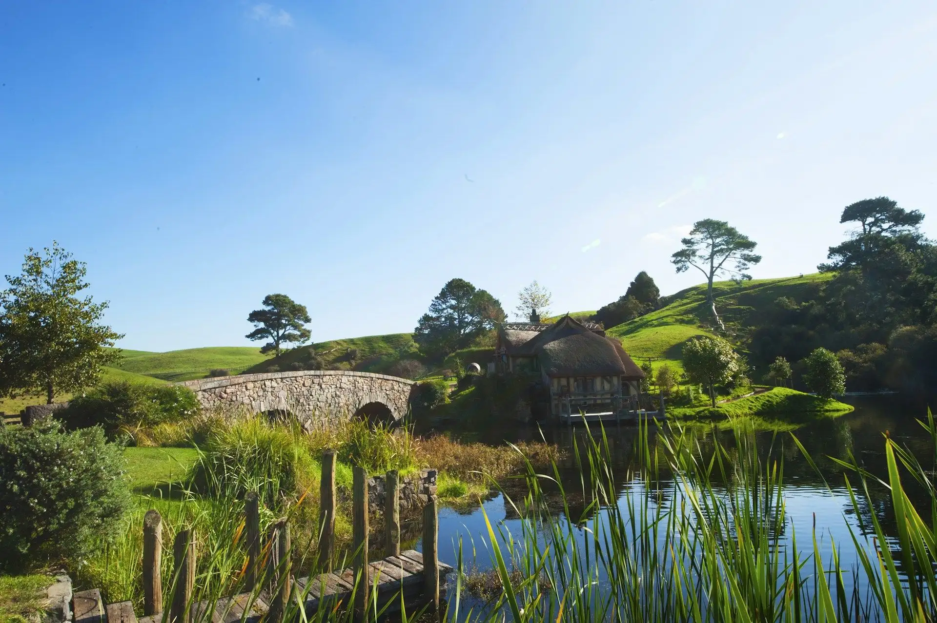The stone bridge and Mill beyond the water at Hobbiton under a blue sky