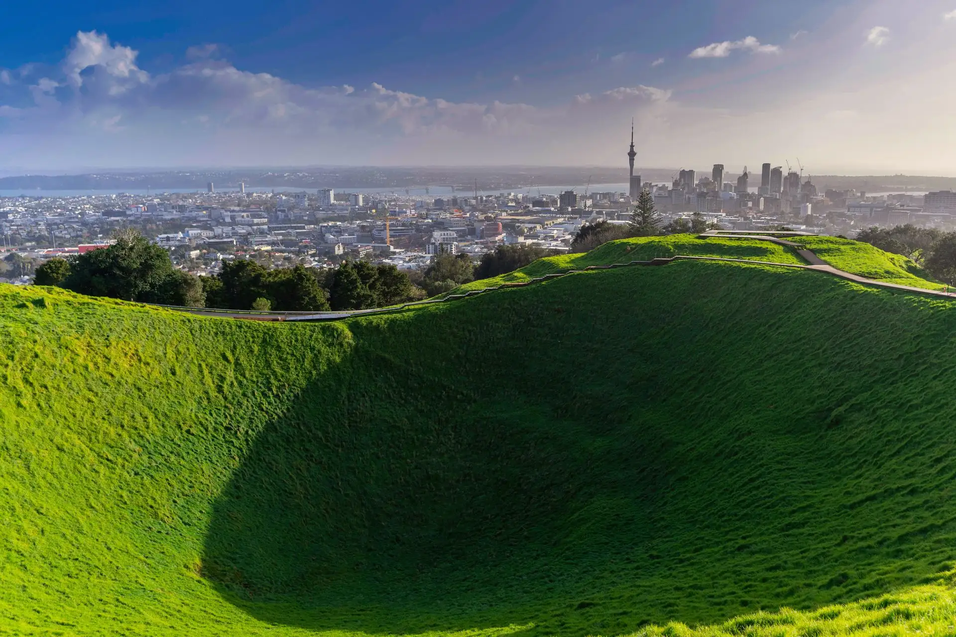 A grassy volcanic crater with the Auckland skyline beyond