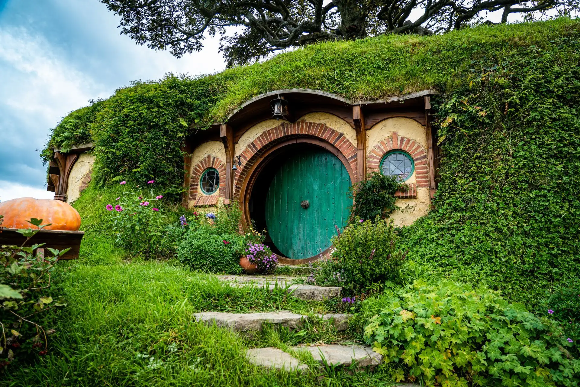 A grass-roofed hobbit hole with a green round door and stone steps at Hobbiton