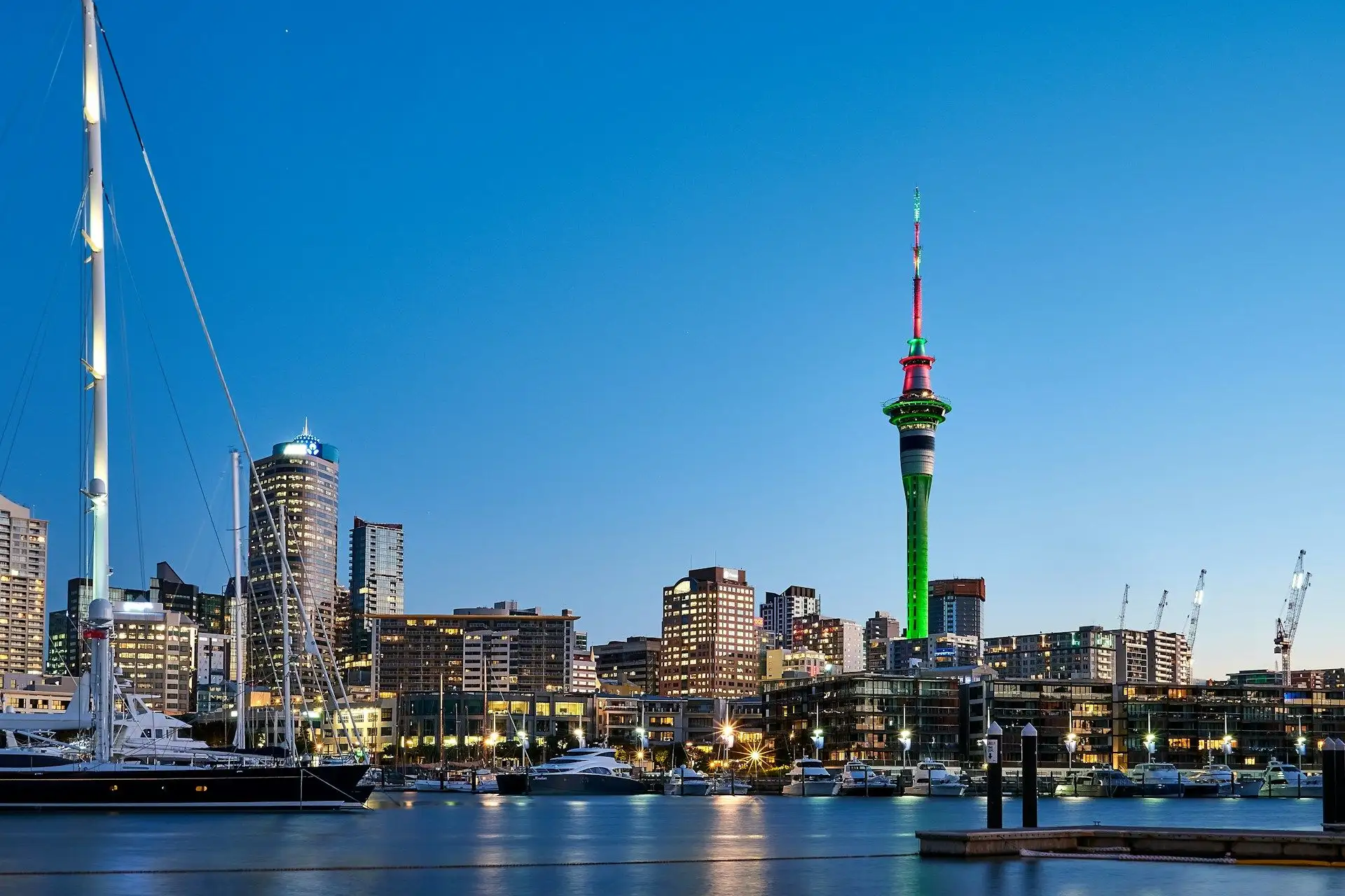 Viaduct Harbour's masts and the lit Sky Tower against a deep blue dusk sky