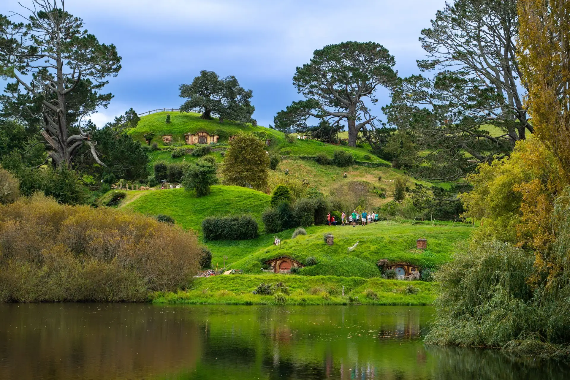 Hobbit holes in a green hillside above the lake at Hobbiton