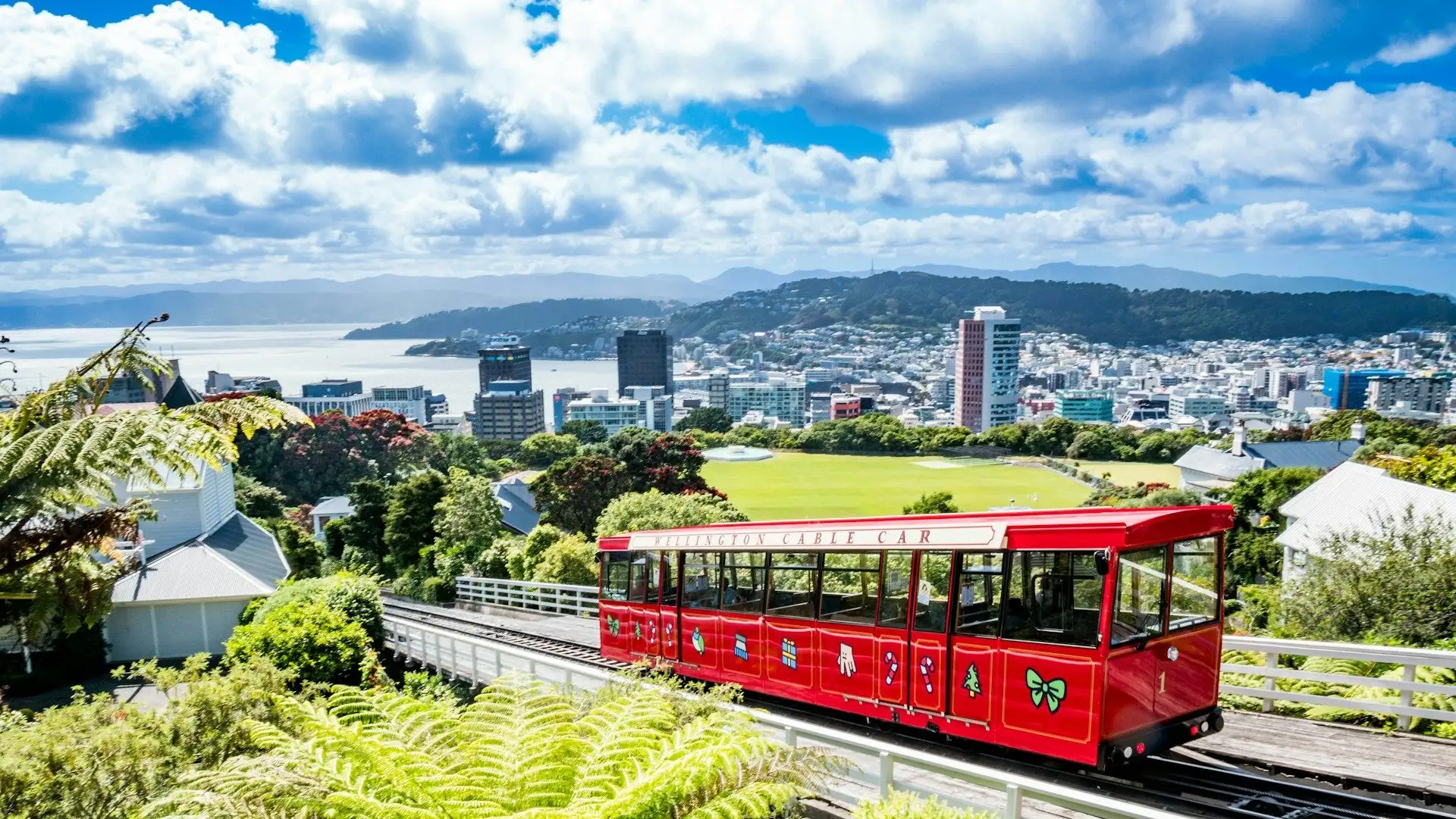 The red Wellington Cable Car above the city and harbour under blue sky with cloud
