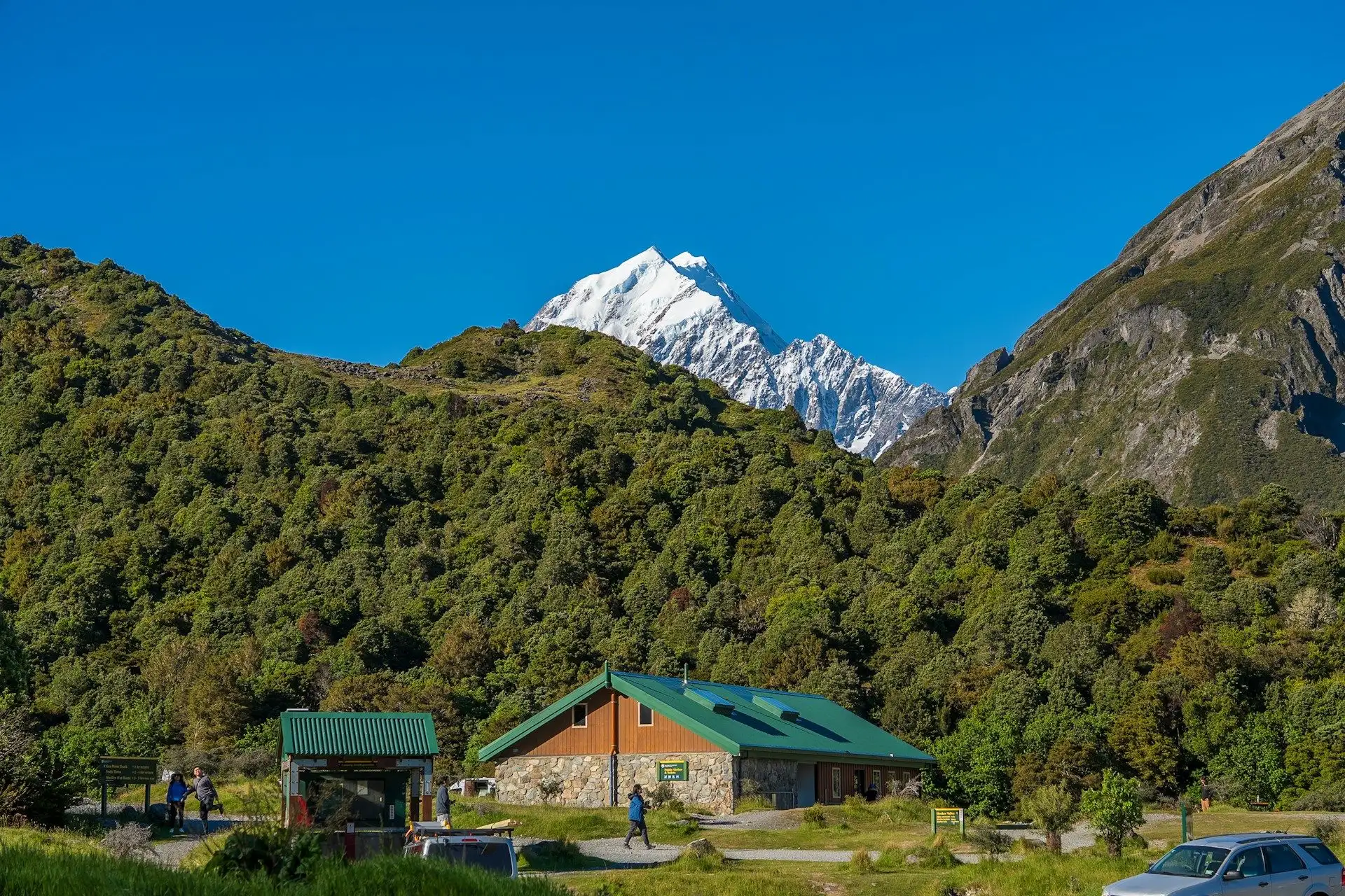 An alpine hut and lodge among bush below snow-capped Aoraki/Mount Cook