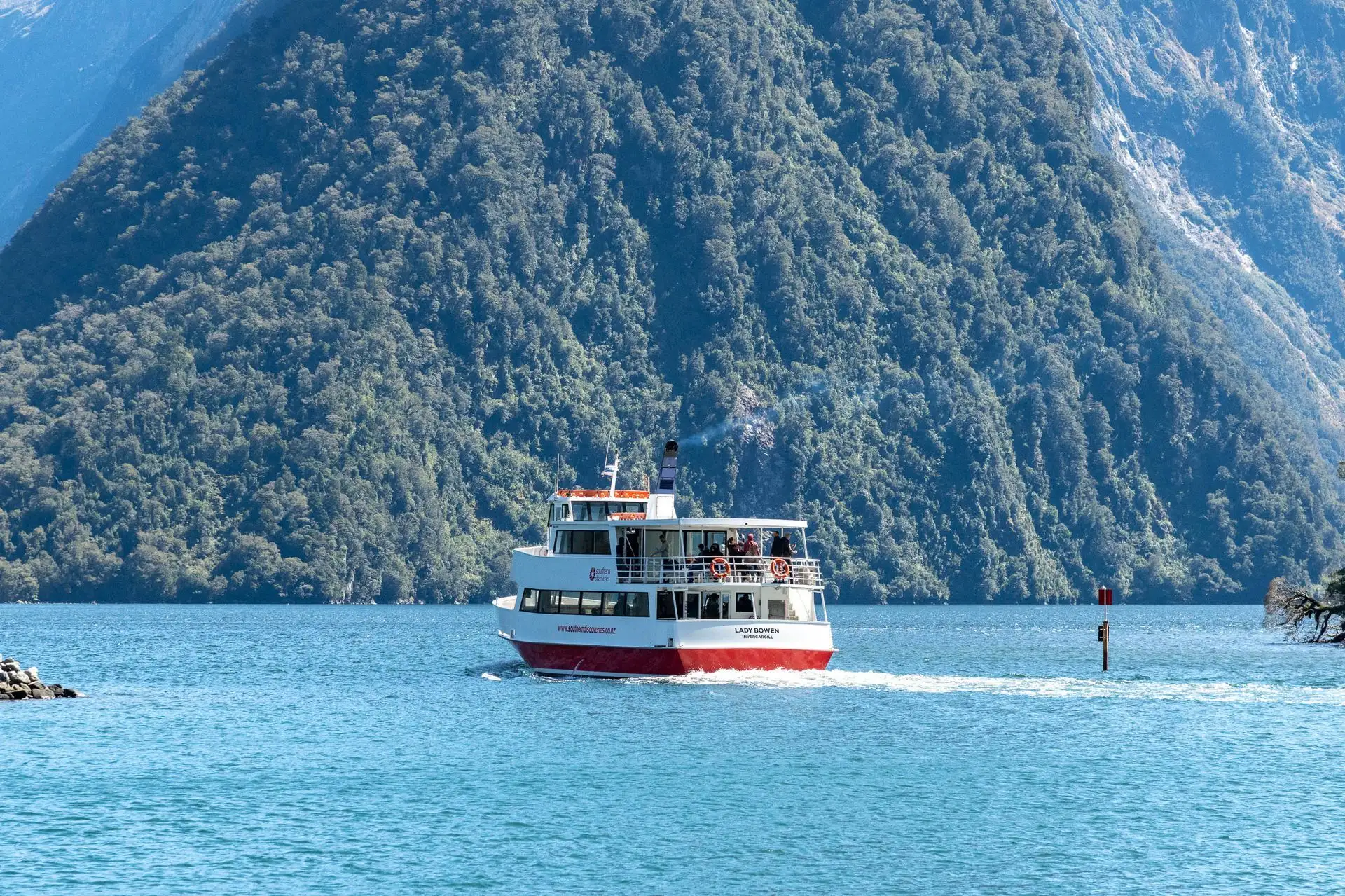 A cruise boat on turquoise water below bush-covered cliffs at Milford Sound