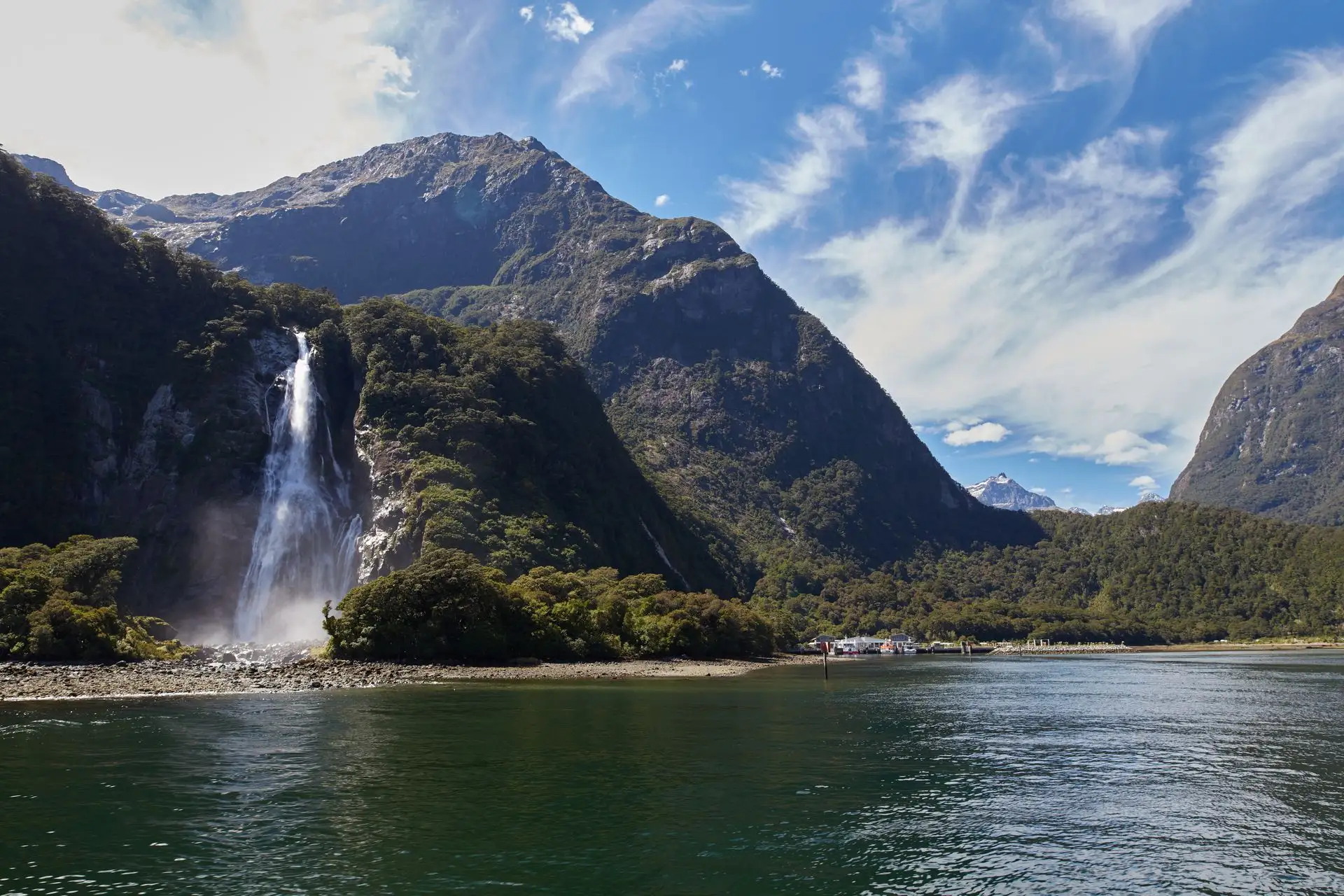 Bowen Falls dropping into Milford Sound under a blue sky with wispy cloud