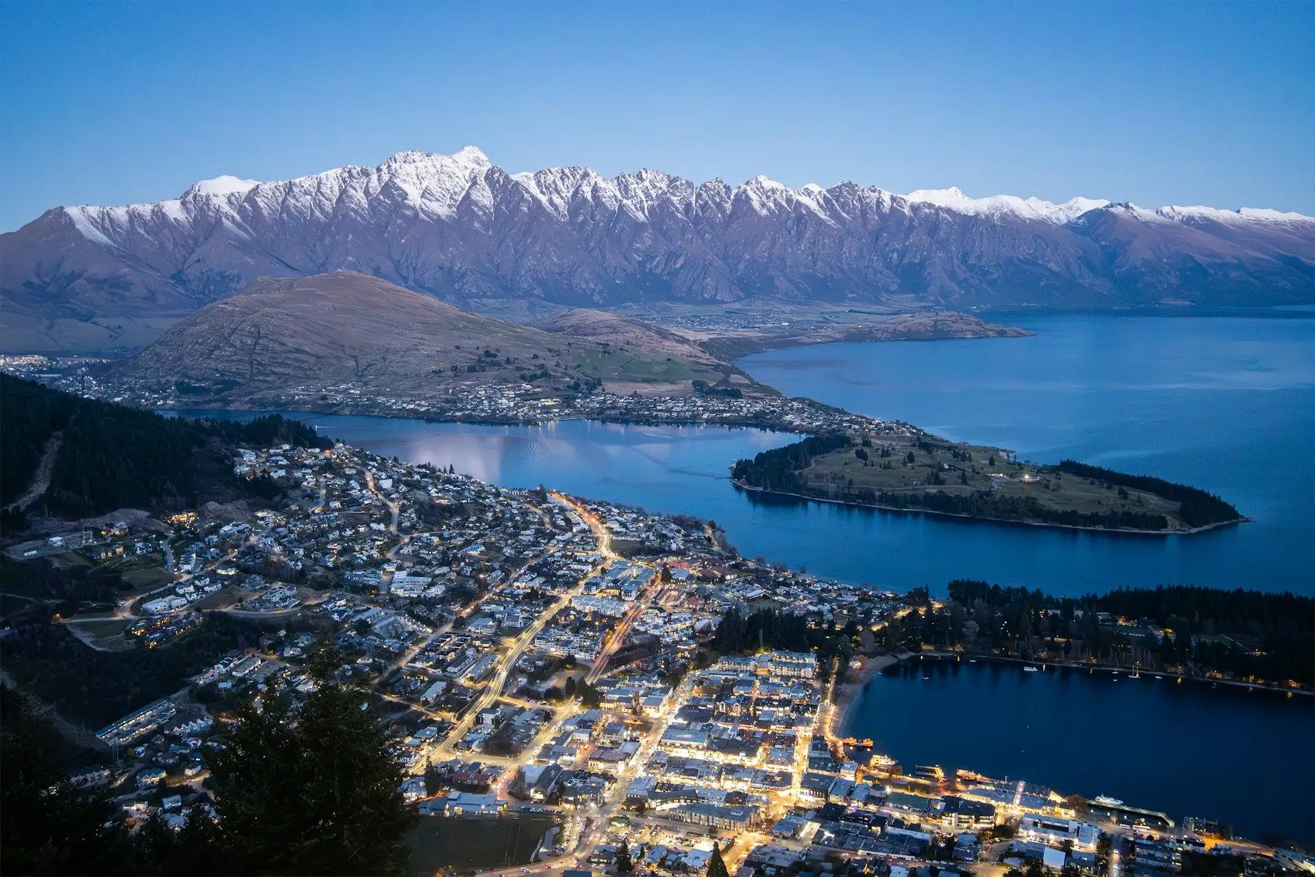 Queenstown's lights at blue hour below the snow-capped Remarkables